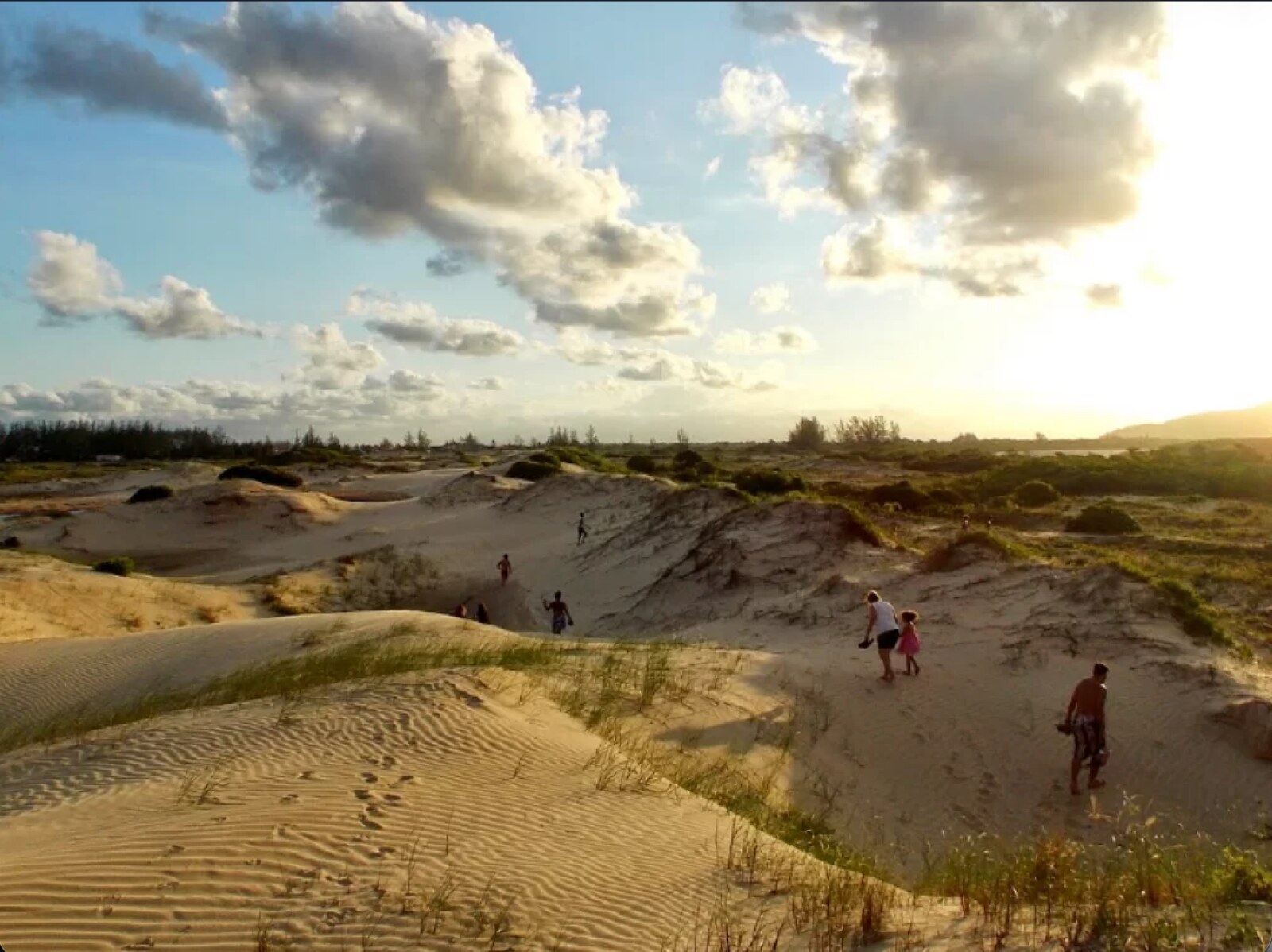 Dunas de areia com vegetação de restinga e visitantes ao pôr do sol em Ilha Comprida