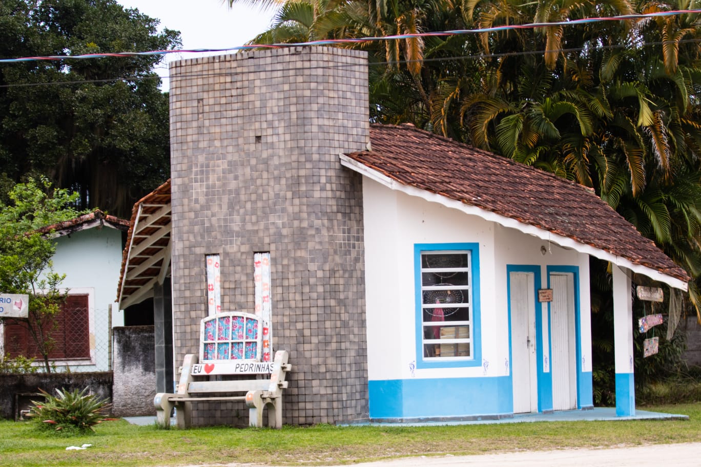 Marco Eu amo Pedrinhas junto a uma construção tradicional da vila